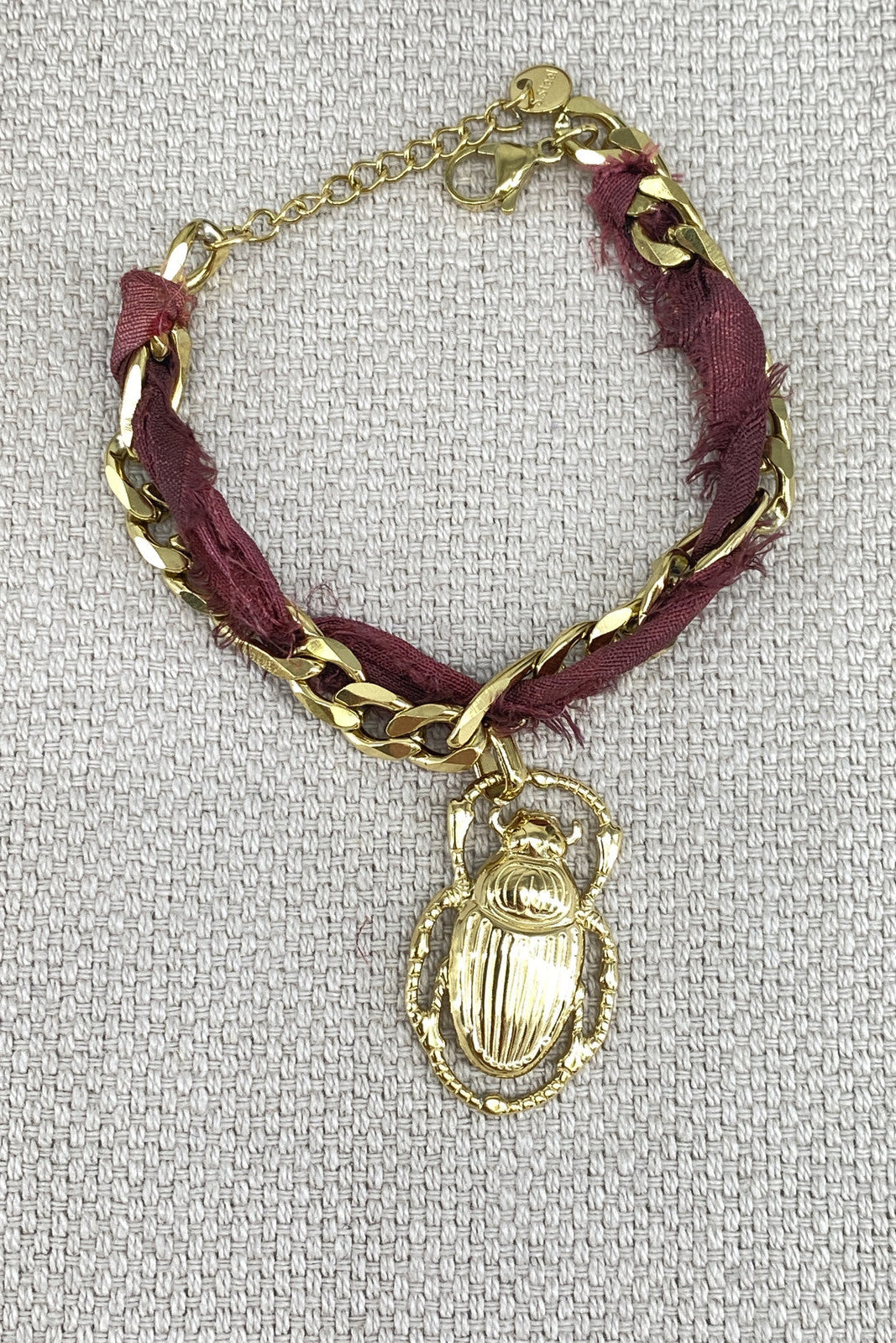 Bracelet with gold chain and scarab charm on a textured 